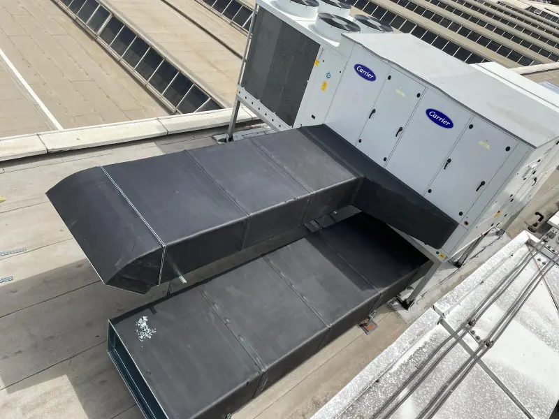 Çatı üzerine monte edilmiş rooftop paket klima cihazına bağlanan siyah izolasyonlu hava kanalı