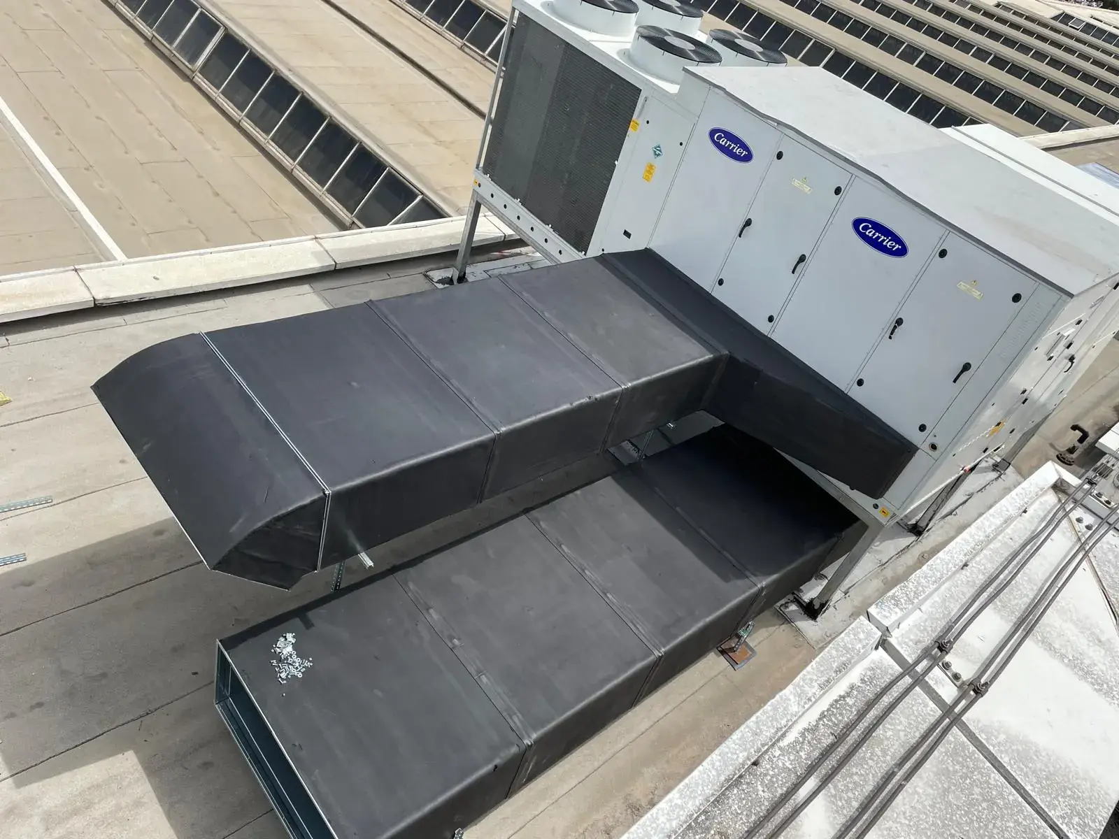 Çatı üzerine monte edilmiş rooftop paket klima cihazına bağlanan siyah izolasyonlu hava kanalı